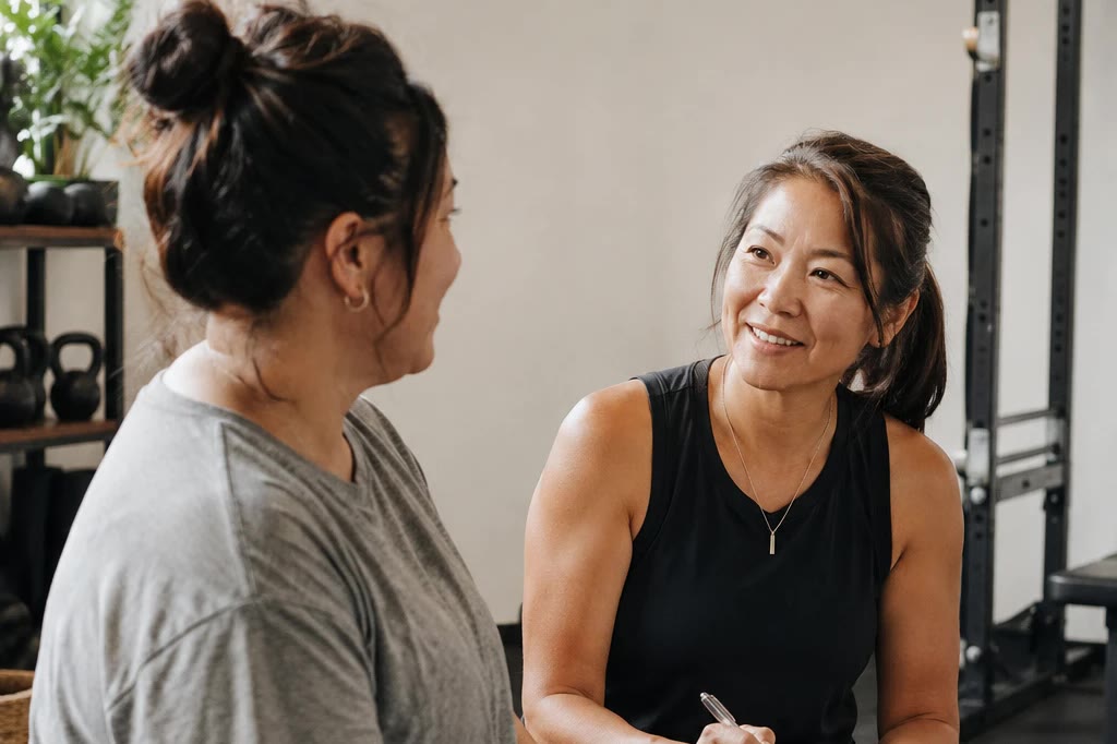 An exercise professional with a notebook, talking with a client in a gym.